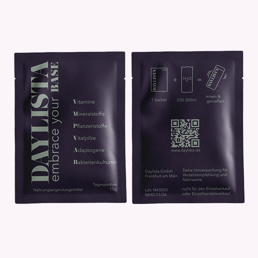 Zwei dunkelviolette Daylista-Sachets nebeneinander: Auf dem linken Beutel stehen vertikal das Logo „DAYLISTA embrace your BASE“ und die Kategorien Vitamine, Mineralstoffe, Pflanzenstoffe, Vitalpilze, Adaptogene und Bakterienkulturen. Der rechte Beutel zeigt Zubereitungshinweise mit Piktogrammen (1 Sachet + Wasser) sowie einen QR-Code und Herstellerinformationen.